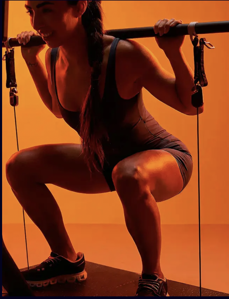Member performing a squat on Lyquid, lit in dramatic orange tones